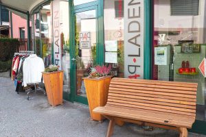 Eingang zum Pongauer ArbeitsProjekt mit Kleidung zur Ansicht und einer Holzbank davor.