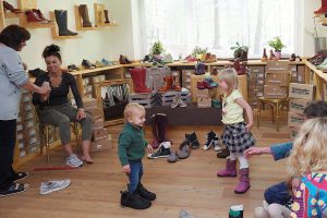 Kinder probieren Schuhe in einem Geschäft, umgeben von vielen Schuhpaaren.