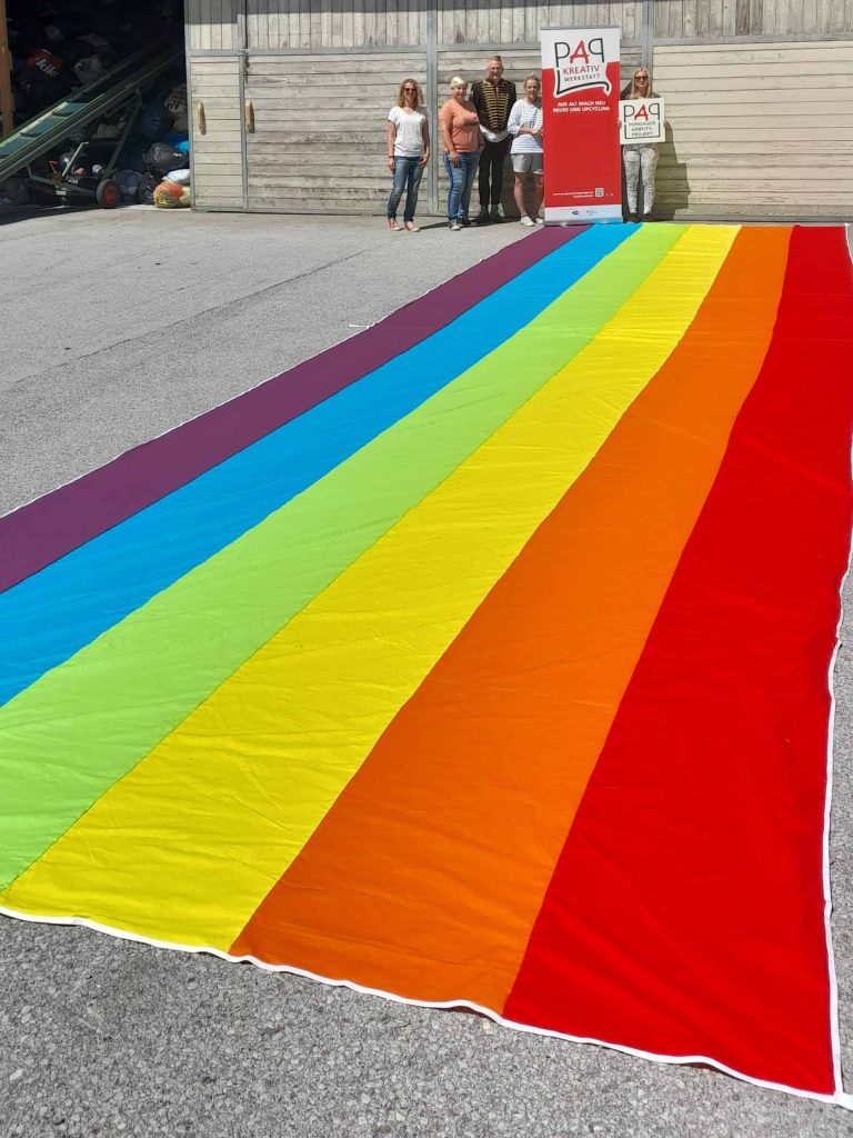 Bunte Regenbogenflagge mit Menschen in der Nähe, Symbol für Vielfalt und Integration.