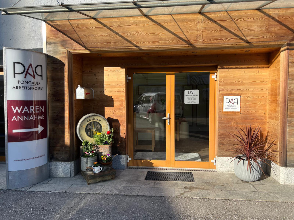 Eingang des Pongauer ArbeitsProjekts mit Schild „Warenannahme“ und verglaster Holztür