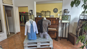 Second-Hand-Verkaufsraum mit zwei Schaufensterpuppen, Kleiderständern und Klavier im Hintergrund