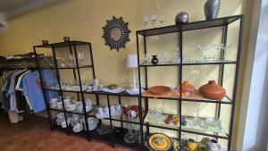 Regale mit Glaswaren, Geschirr und Deko neben einem Kleiderständer in einem Second-Hand-Verkaufsraum